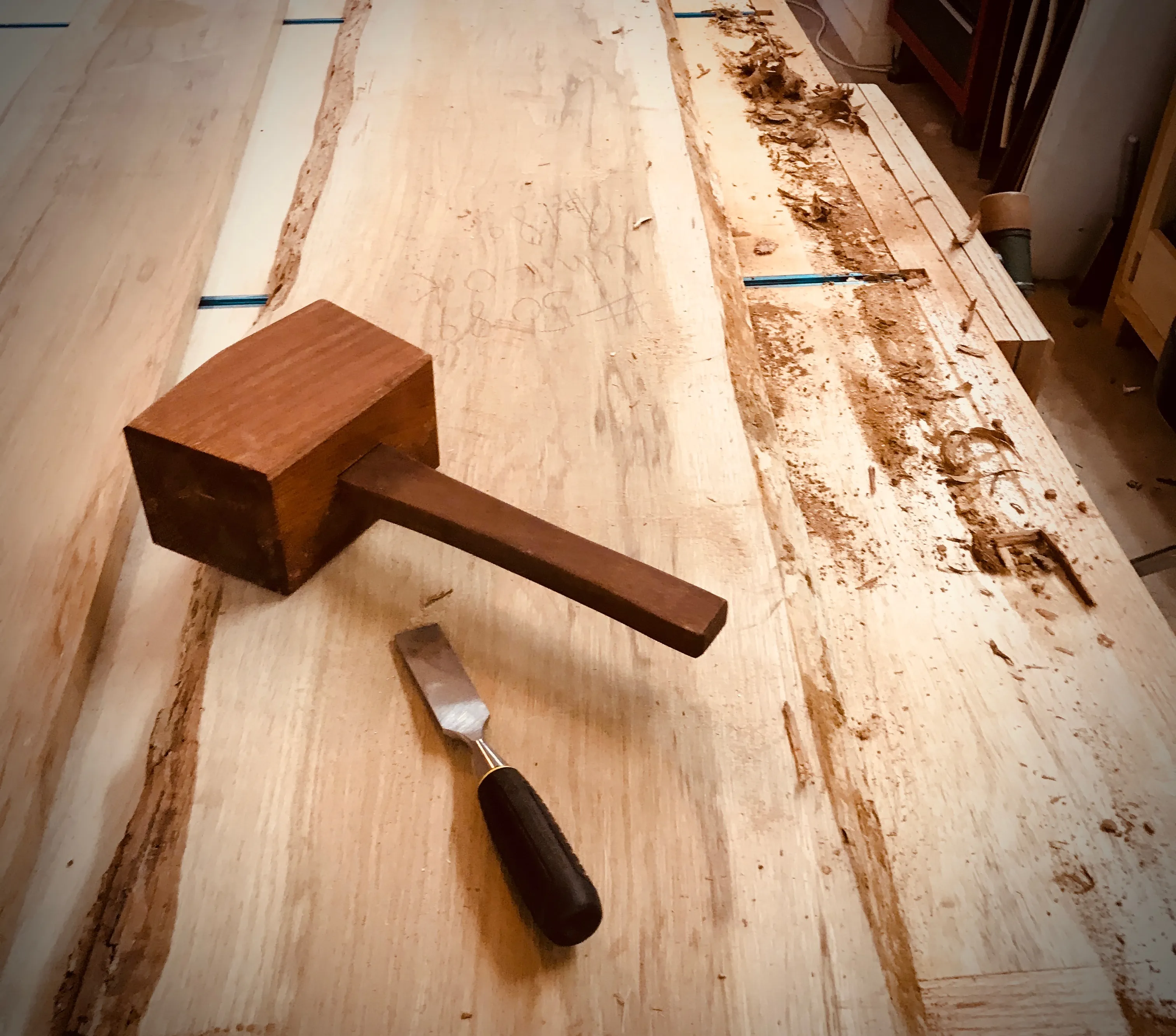 Wooden mallet and chisel resting on a rough-sawn white oak slab, used for the bed's mortise and tenon joinery