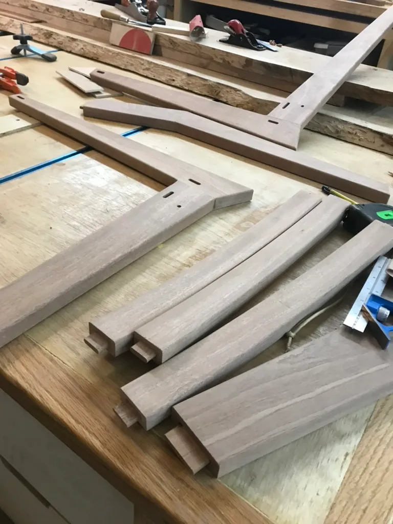 Mahogany mortise and tenon leg and seat frame pieces cut and laid out on the workbench