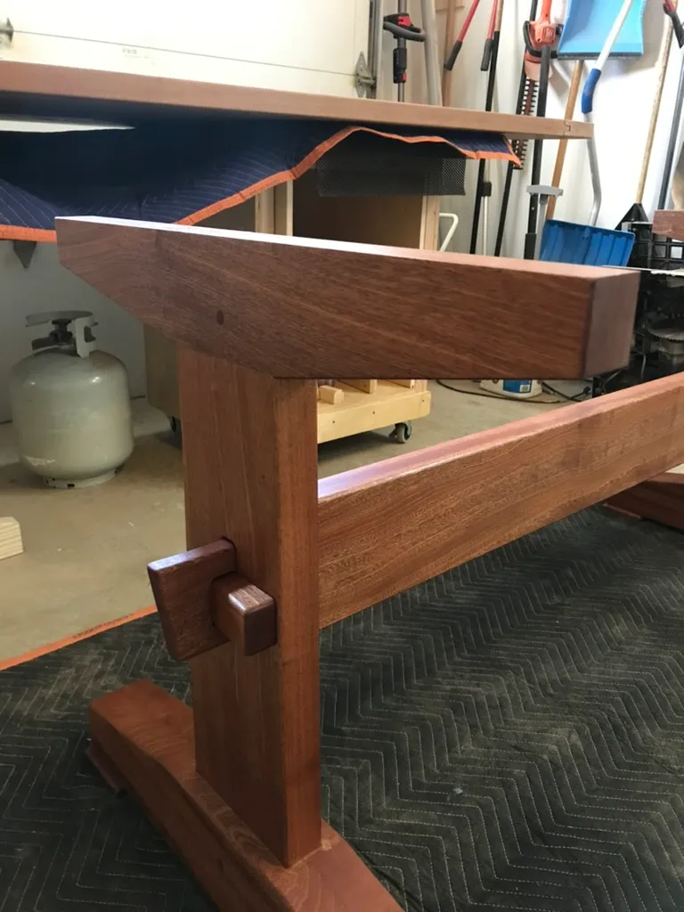 Close-up of the finished trestle table's mortise and tenon joint with a wedged key, at the leg-to-stretcher connection