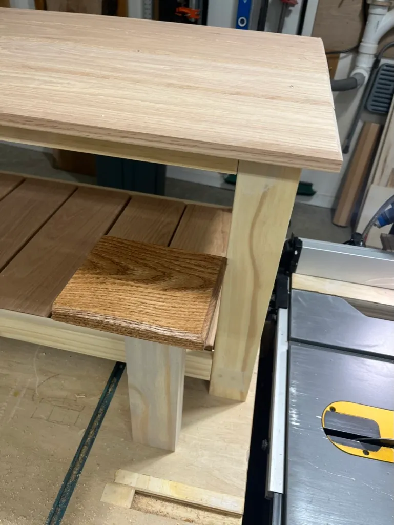 Close-up of a small oak inlay block being fit into the coffee table's shelf edge, on the sawhorse