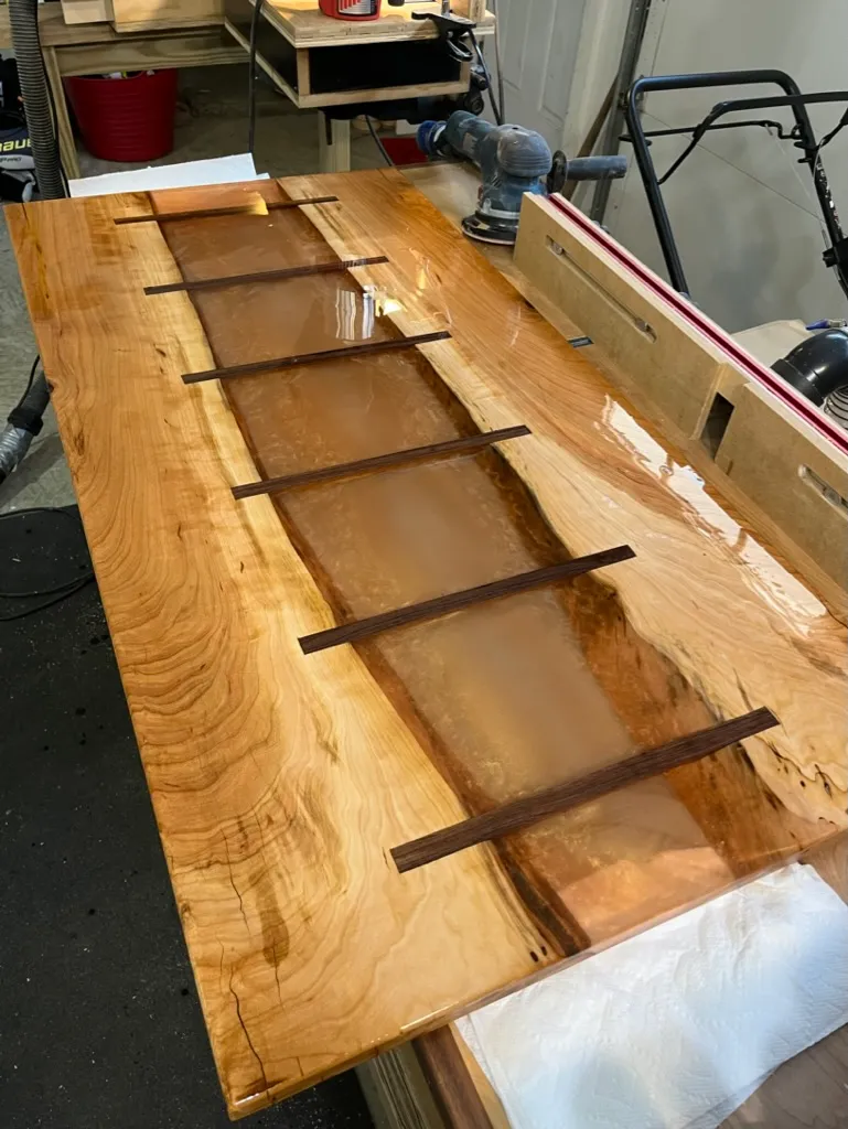 Finished river table tabletop with amber epoxy inlay strips, curing under plastic wrap on sawhorses