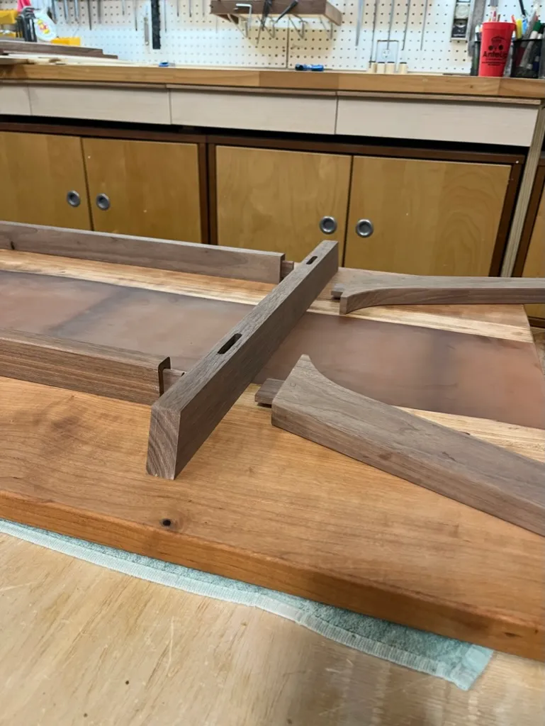 Walnut trestle-style table base and legs assembled, no tabletop yet, standing in the shop