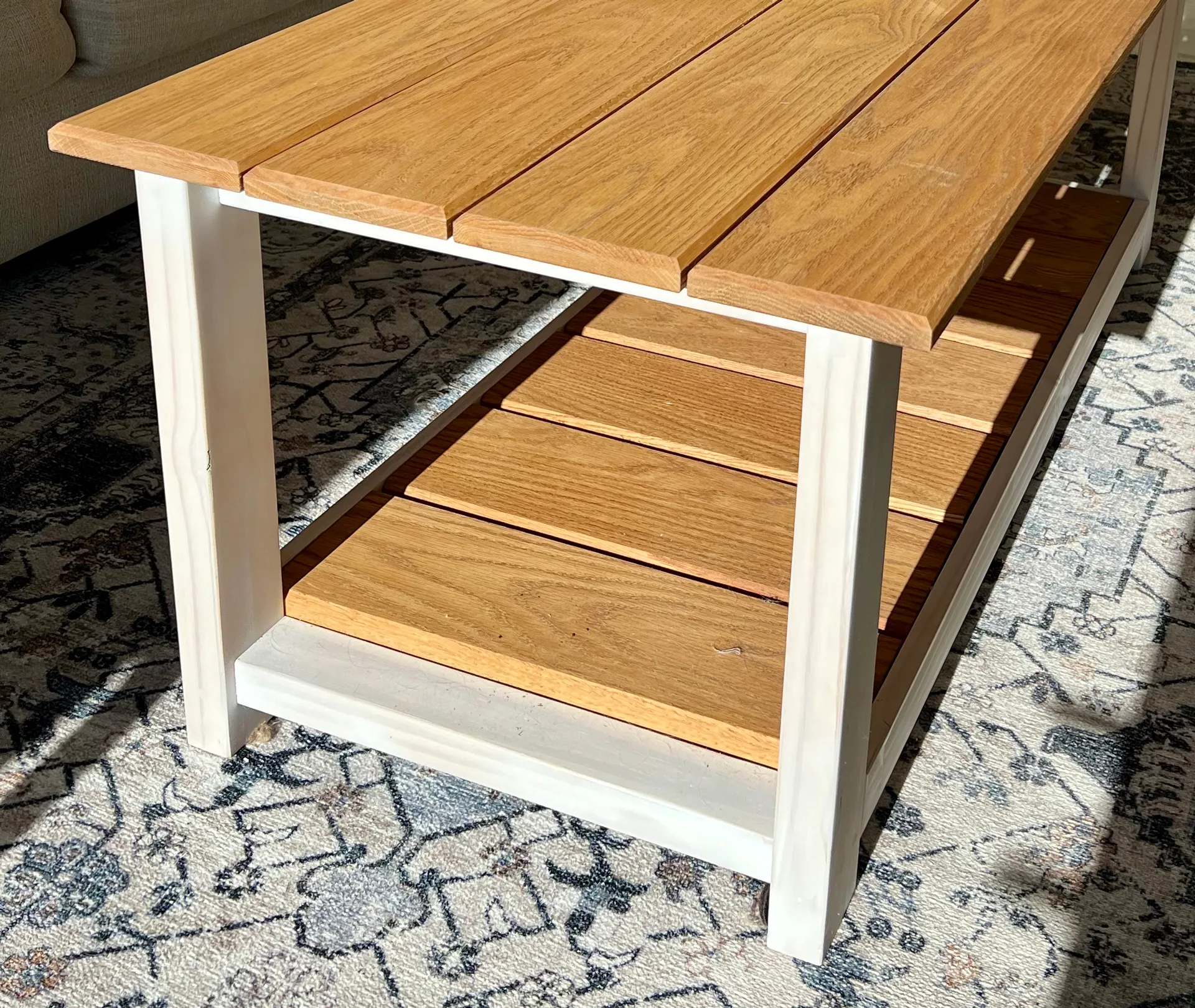 Close-up corner of the white oak coffee table, showing the slatted lower shelf and light stain, on a patterned rug