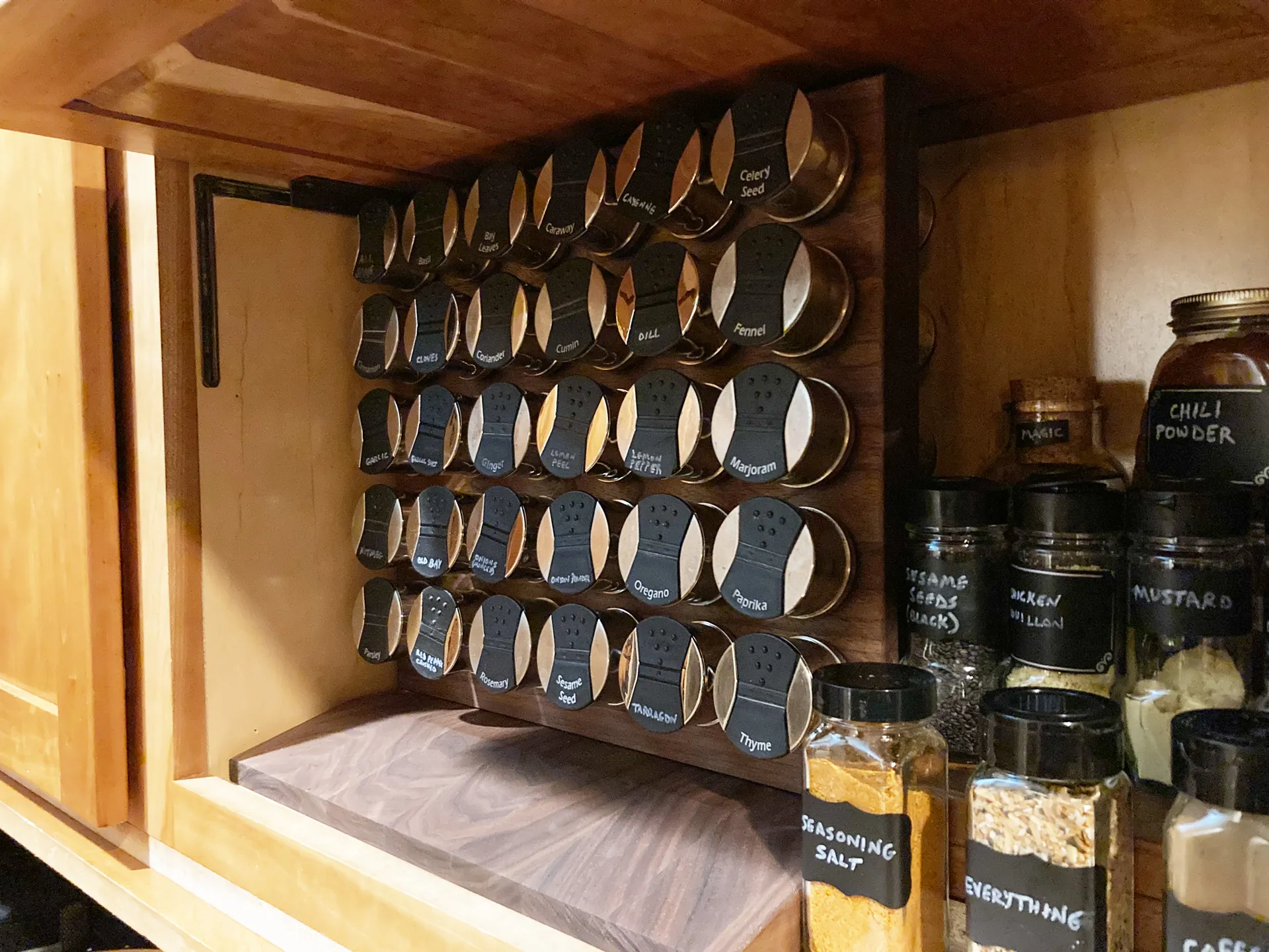 Finished walnut spice rack mounted in a cabinet, fully loaded with 30 labeled spice tins