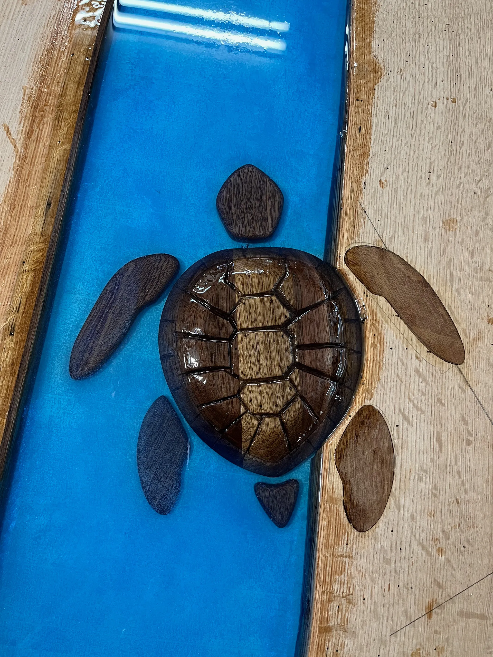 Close-up detail of the carved wood sea turtle inlay pieces, shell and flippers, set into the blue epoxy before the final pour