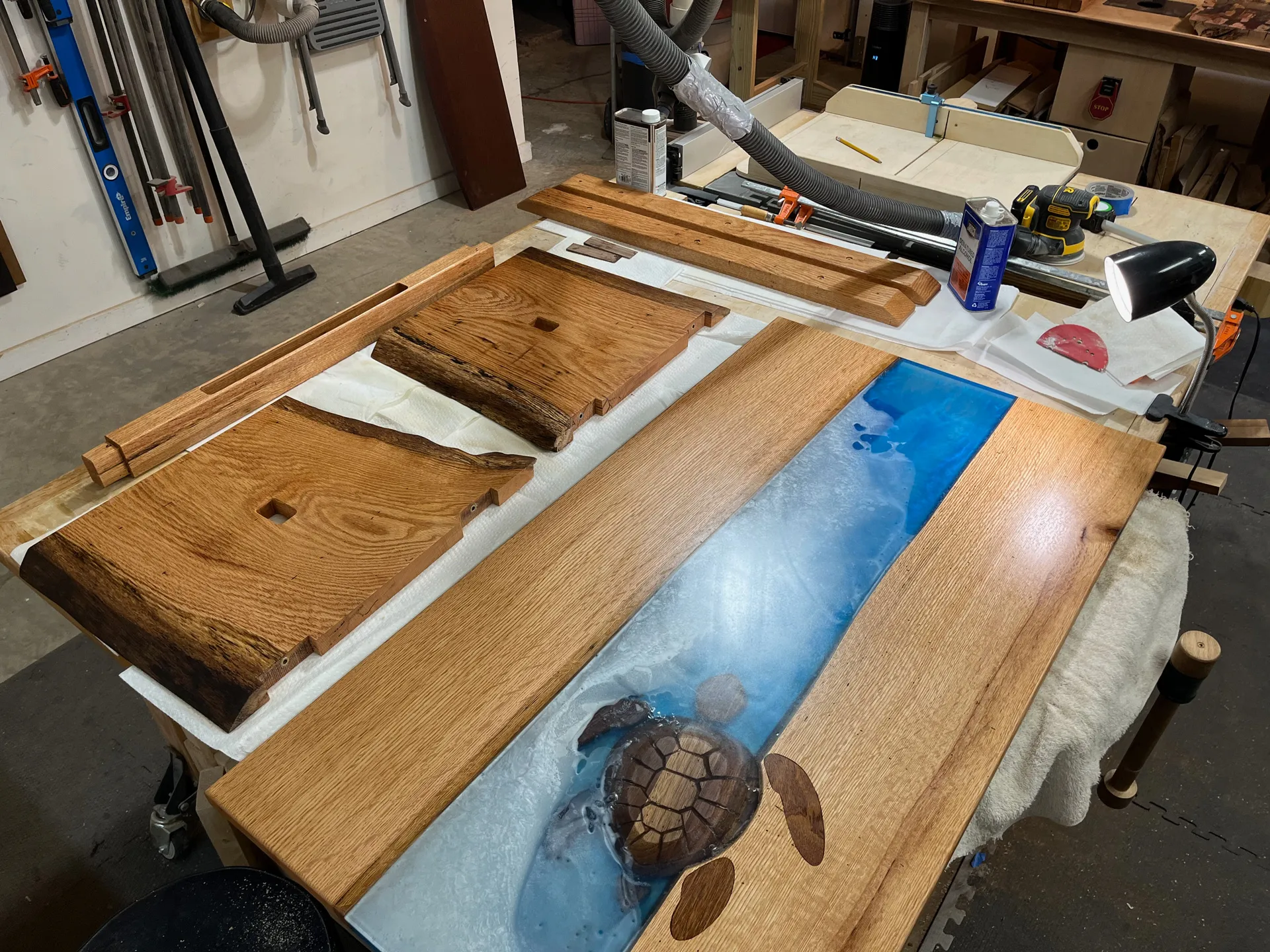 In-progress shot of the turtle table's raw oak pieces, a corner clamp, and the blue epoxy river with the turtle inlay partially complete, in the shop