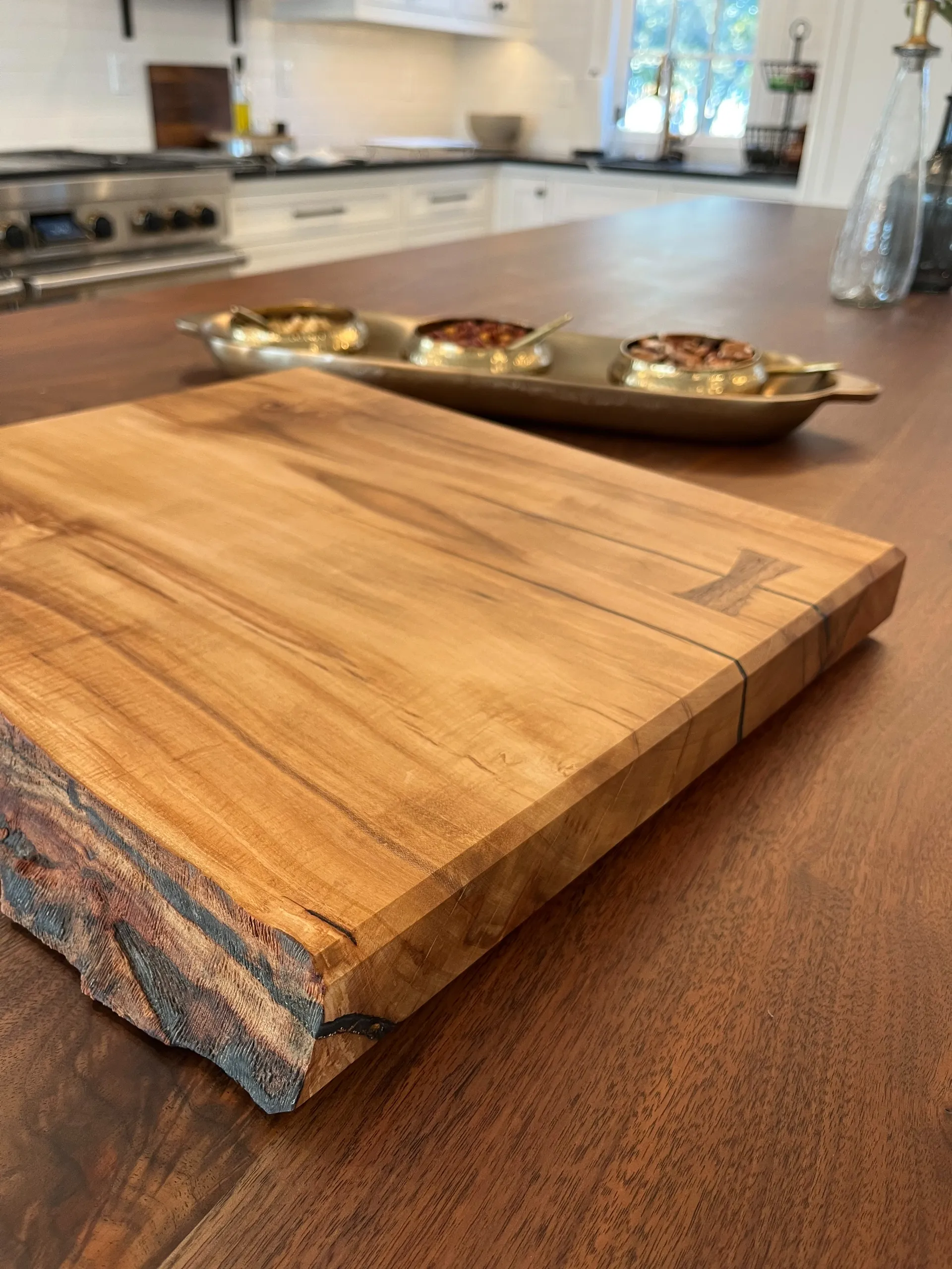Finished live edge sugar maple cutting board with a bowtie inlay, on a kitchen island near small serving bowls