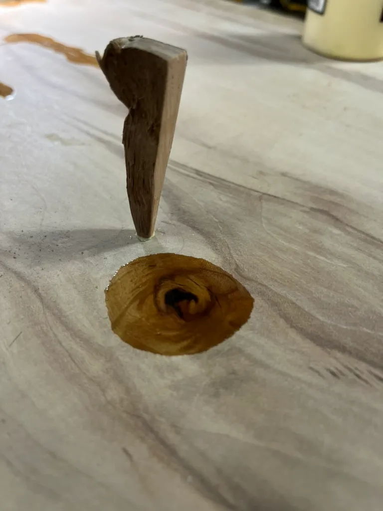 Epoxy-filled knot in the cutting board with a carved wood plug set above it, mid-repair