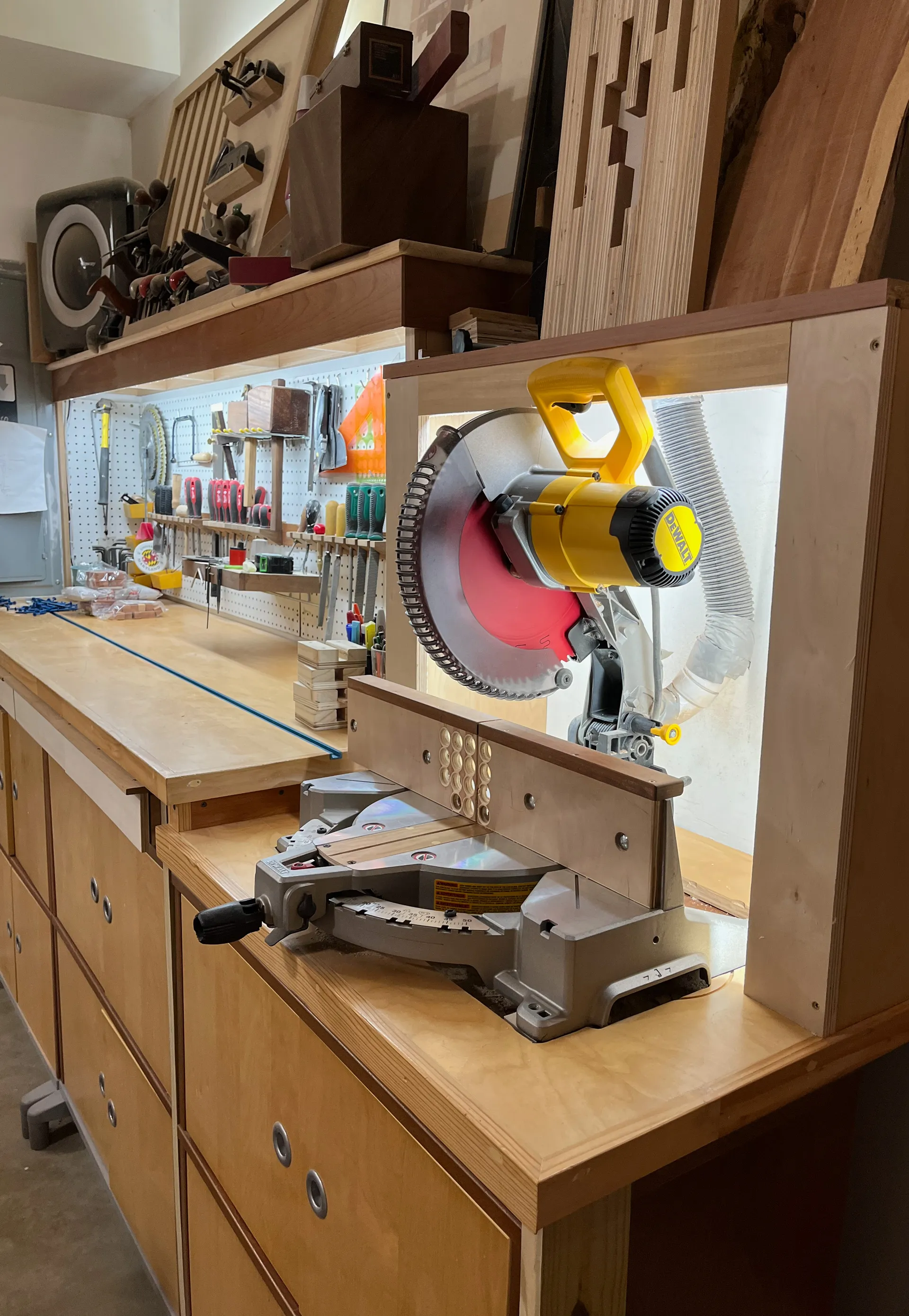 Wall-mounted rack of vintage hand planes above a workbench with a mitre saw station, chisels, and mallets hung on a pegboard