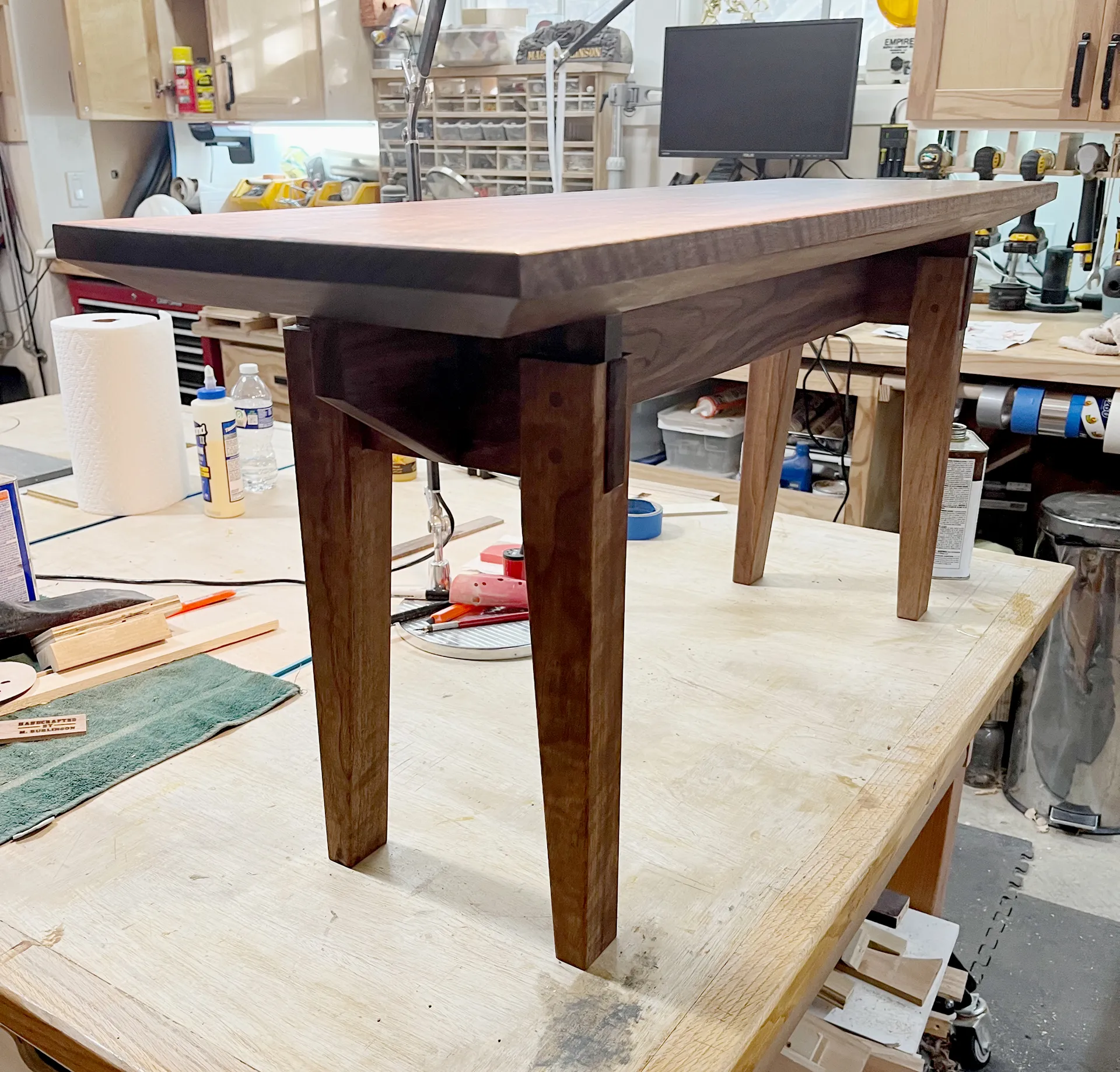 Finished walnut entryway bench staged on the workbench in the shop, dark stain applied, before delivery