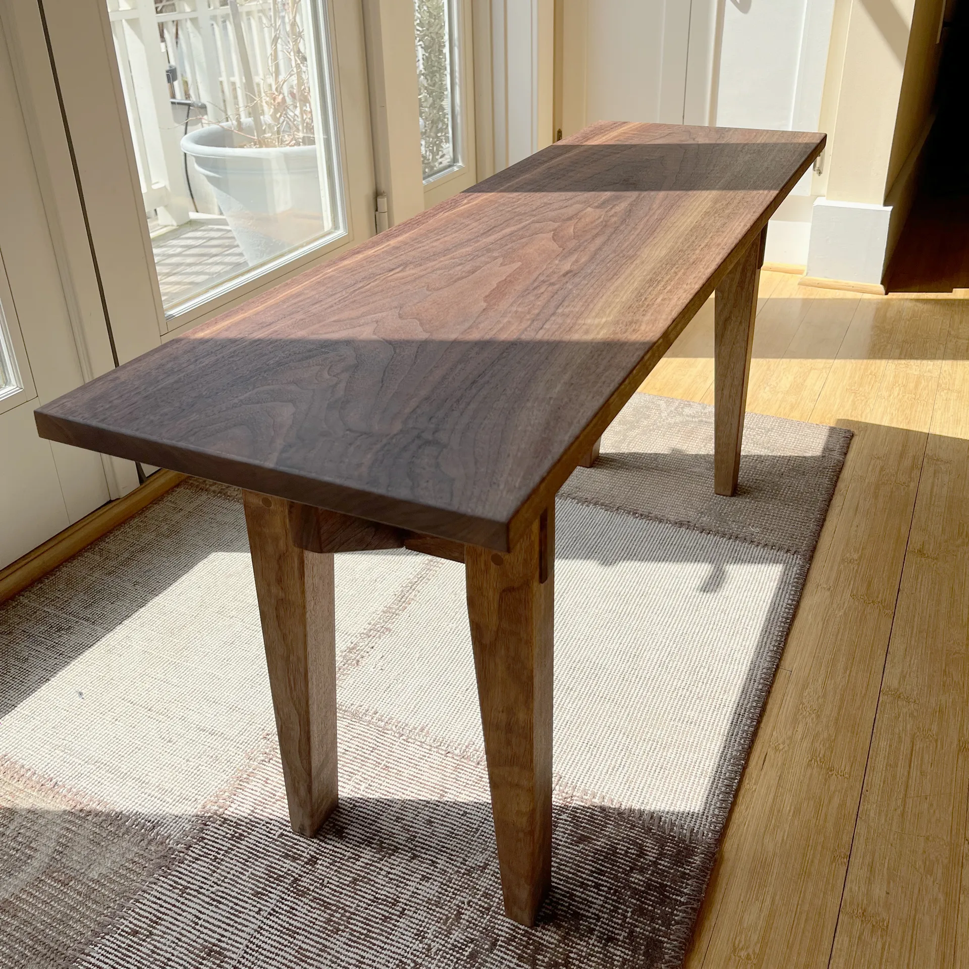 Finished walnut entryway bench in a sunlit room with a potted plant and glass doors