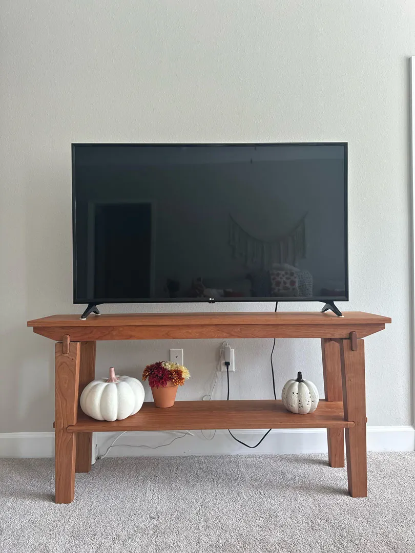 Finished cherry end table under a wall-mounted TV, styled with pumpkins and flowers for fall