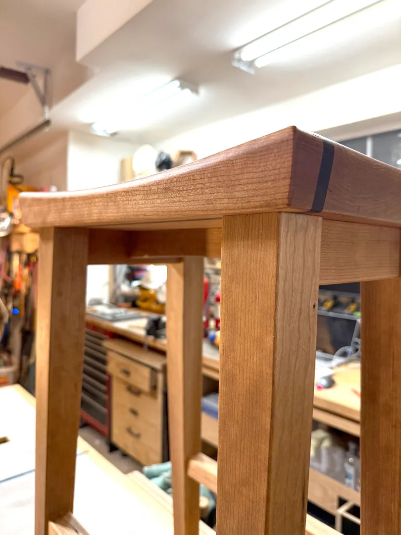 Side view of a cherry bar stool showing its tapered legs